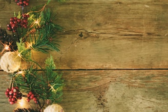 A rustic wooden surface adorned with festive decorations on the side, including pine branches, red berries, pinecones, and glowing lights, creating a seasonal and natural atmosphere.
