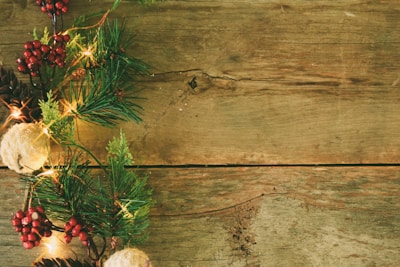 A rustic wooden surface adorned with festive decorations on the side, including pine branches, red berries, pinecones, and glowing lights, creating a seasonal and natural atmosphere.