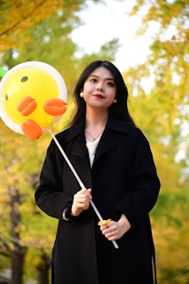 A joyful woman smiling while holding a heart-shaped balloon in a sunny park.