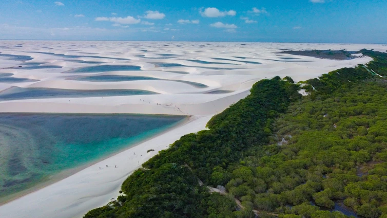 A vibrant sunset over the white dunes and turquoise lagoons of Lençóis Maranhenses, with a local guide leading a small group of travelers.