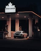 A car is parked at a gas station at night, illuminated by the overhead lights. The station displays a Petro-Canada sign and offers self-service fuel pumps.
