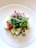 A colorful and vibrant salad arranged on a white plate. The salad consists of a mix of green leafy vegetables, small cubes of different fruits and vegetables such as apples and melons, as well as cherry tomatoes. On top, there are fine strips of radishes. The white plate and the natural lighting highlight the freshness of the ingredients.