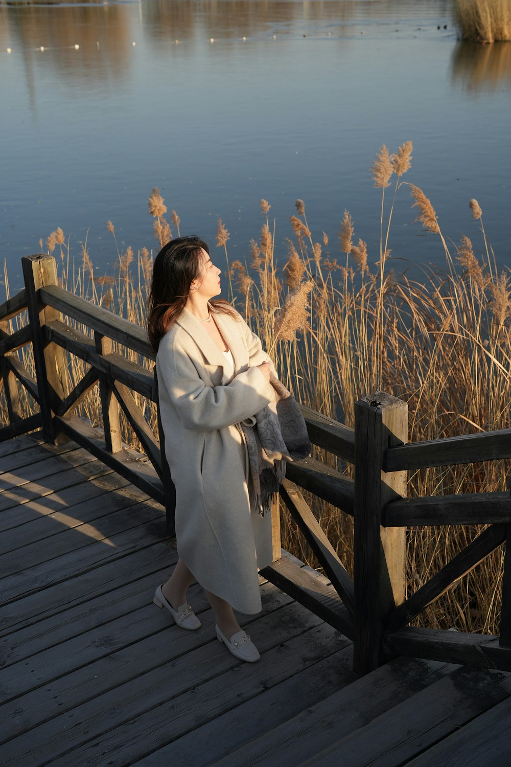 a woman standing on a wooden bridge next to a body of water