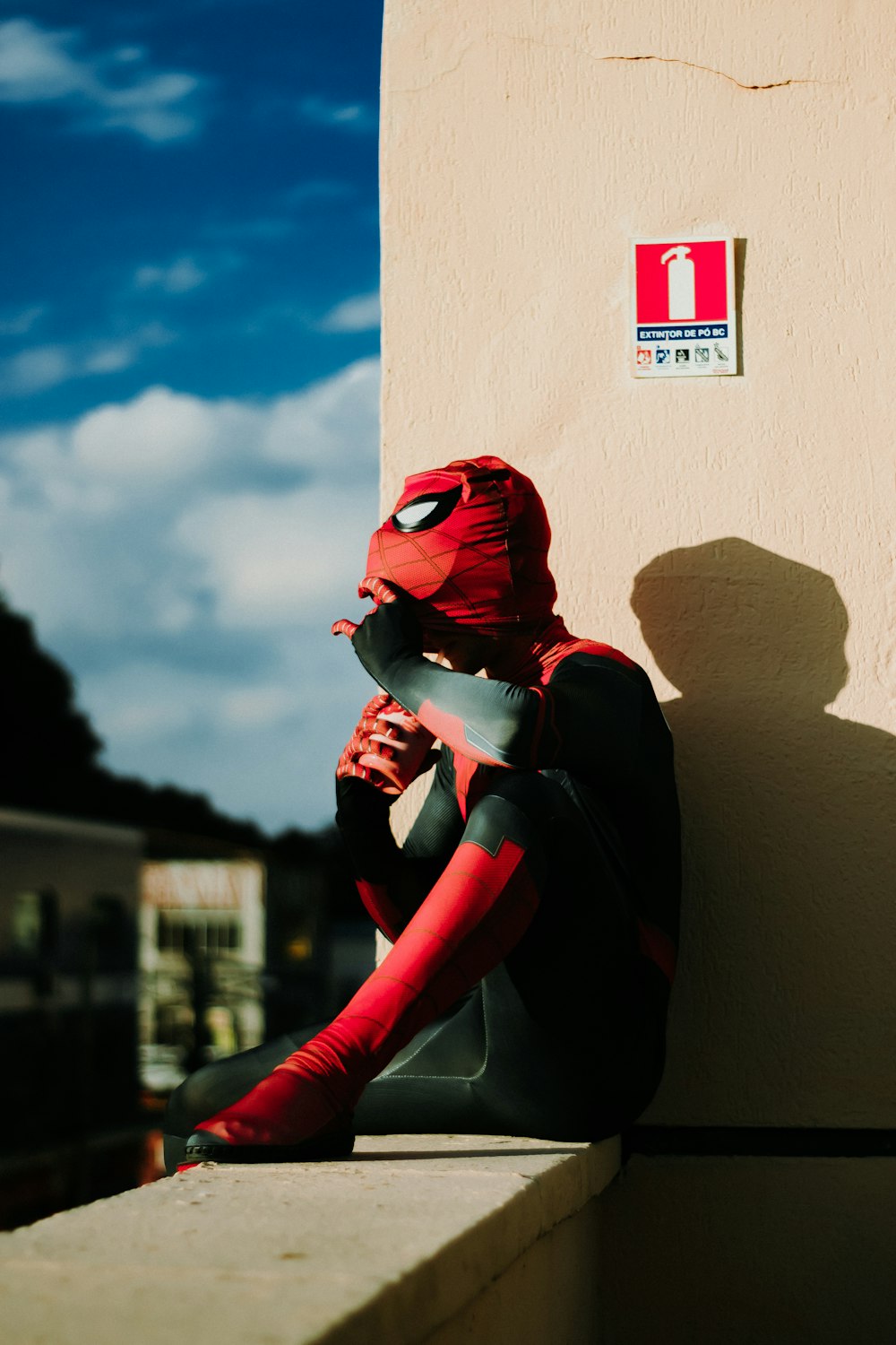 a person with a red mask sitting on a ledge