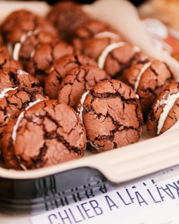 A tray filled with chocolate sandwich cookies, each featuring a creamy white filling. The cookies exhibit a distinctive cracked surface, revealing their rich brown color and texture. The background includes partially visible text, suggesting a display setting.