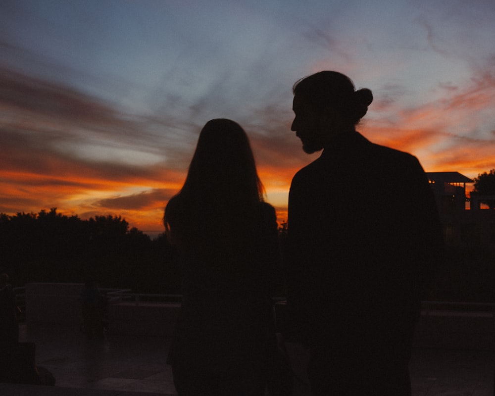 a man and a woman standing in front of a sunset