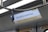 A train interior with a sign displaying 'Lok Ma Chau' alongside safety messages in English and Chinese, including 'Please mind the gap.' The ceiling features a metallic handrail with a blue handle for standing passengers.