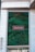 A vertical garden is integrated into the facade of a building, featuring lush green foliage. A rectangular sign with white script is centrally positioned on the garden wall. The exterior is made of light-colored stone tiles, complementing the natural green hues of the plants.