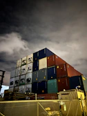Stacked shipping containers in shades of blue and gray under moody lighting.