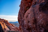 A climber scaling a sunlit sandstone cliff with a vast blue sky backdrop.
