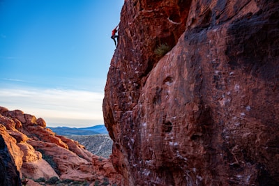 A climber scaling a sunlit sandstone cliff with a vast blue sky backdrop.