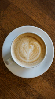 Steaming cup of specialty coffee with a beautiful latte art heart on a vintage ceramic saucer.