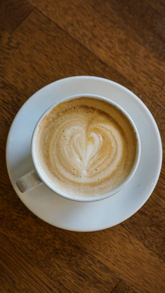 Steaming cup of specialty coffee with a beautiful latte art heart on a vintage ceramic saucer.