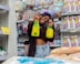 Smiling woman holding a box of products in a small retail store.