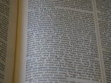 An open book displaying text with clear black font on a cream-colored page. The text is formatted in two columns, and the focus is on the central text, with parts slightly blurred on the edges.