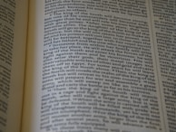 An open book displaying text with clear black font on a cream-colored page. The text is formatted in two columns, and the focus is on the central text, with parts slightly blurred on the edges.