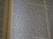 An open book displaying text with clear black font on a cream-colored page. The text is formatted in two columns, and the focus is on the central text, with parts slightly blurred on the edges.