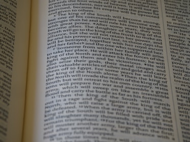 An open book displaying text with clear black font on a cream-colored page. The text is formatted in two columns, and the focus is on the central text, with parts slightly blurred on the edges.