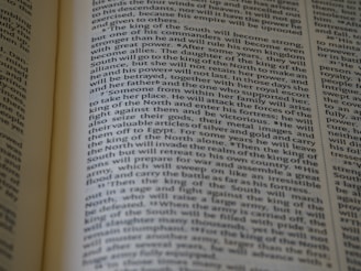 An open book displaying text with clear black font on a cream-colored page. The text is formatted in two columns, and the focus is on the central text, with parts slightly blurred on the edges.
