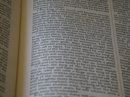 An open book displaying text with clear black font on a cream-colored page. The text is formatted in two columns, and the focus is on the central text, with parts slightly blurred on the edges.
