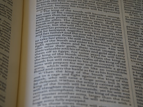 An open book displaying text with clear black font on a cream-colored page. The text is formatted in two columns, and the focus is on the central text, with parts slightly blurred on the edges.