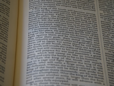 An open book displaying text with clear black font on a cream-colored page. The text is formatted in two columns, and the focus is on the central text, with parts slightly blurred on the edges.