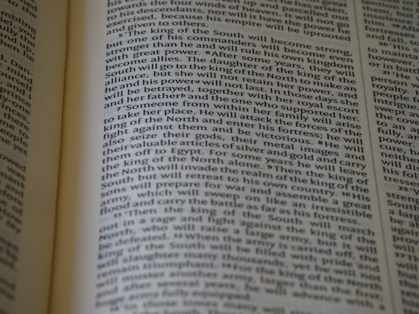 An open book displaying text with clear black font on a cream-colored page. The text is formatted in two columns, and the focus is on the central text, with parts slightly blurred on the edges.