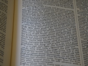 An open book displaying text with clear black font on a cream-colored page. The text is formatted in two columns, and the focus is on the central text, with parts slightly blurred on the edges.