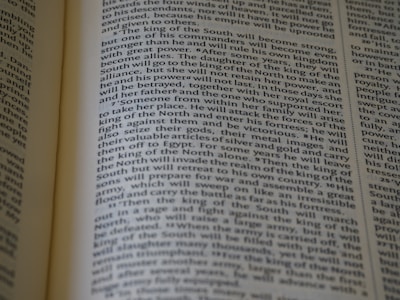 An open book displaying text with clear black font on a cream-colored page. The text is formatted in two columns, and the focus is on the central text, with parts slightly blurred on the edges.