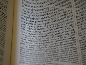 An open book displaying text with clear black font on a cream-colored page. The text is formatted in two columns, and the focus is on the central text, with parts slightly blurred on the edges.