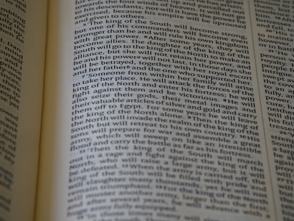 An open book displaying text with clear black font on a cream-colored page. The text is formatted in two columns, and the focus is on the central text, with parts slightly blurred on the edges.