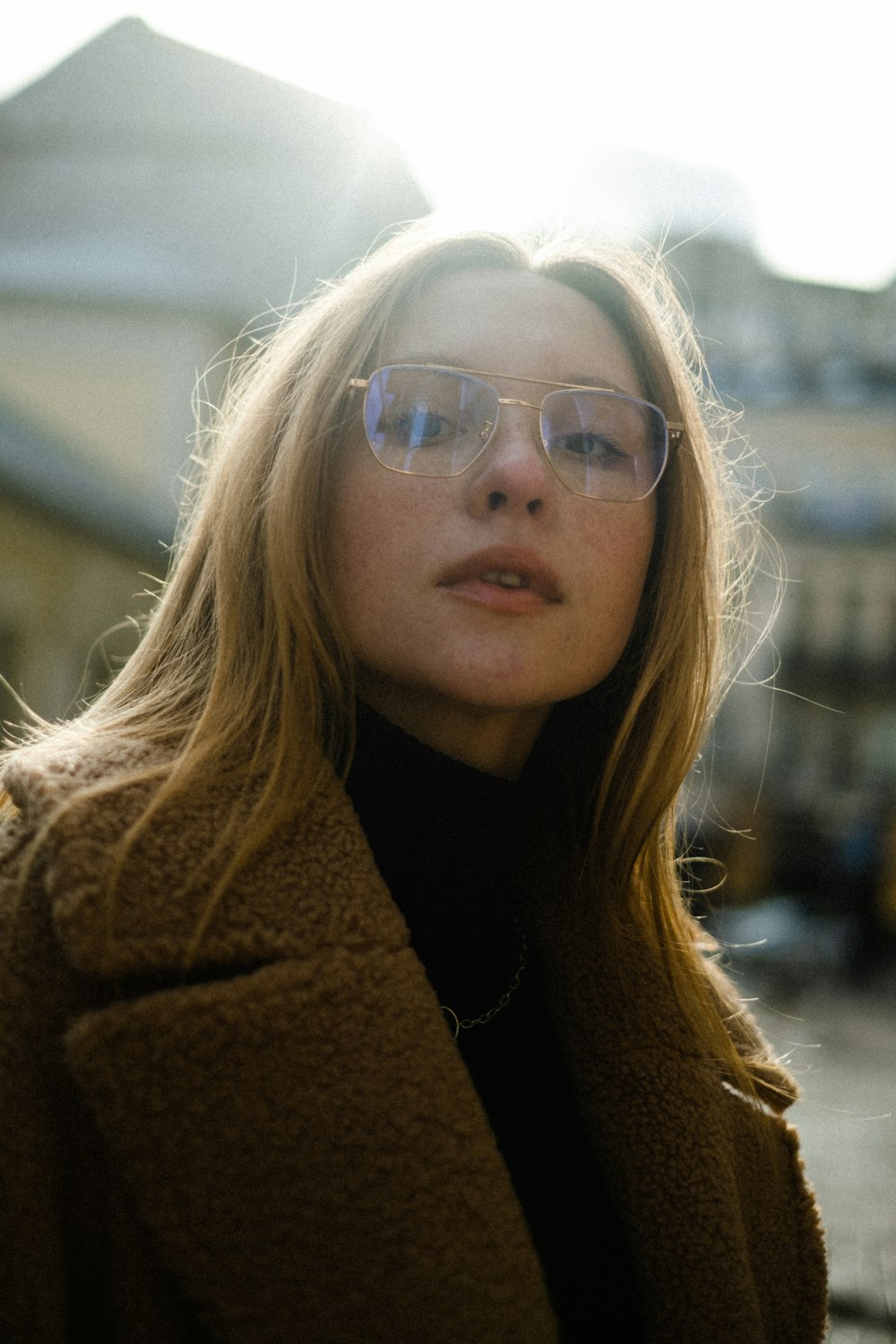 a woman wearing glasses standing in front of a building