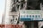 A busy urban street with high-rise residential buildings in the background. Various signs are displayed prominently, including one for 'New York Chiropractic' in both English and Chinese. Another sign is in Chinese characters, and there are several balconies with hanging laundry.