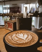 A close-up of a coffee cup with latte art on a wooden table next to a menu.