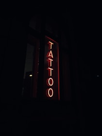 A neon sign with the word 'TATTOO' in bold red letters vertically placed against a dark background.