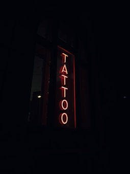 A neon sign with the word 'TATTOO' in bold red letters vertically placed against a dark background.