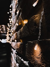 A close-up view of a brick wall adorned with warm white string lights, creating a cozy and inviting atmosphere. The lights are blurred in the background, enhancing the depth and focus on the wall.