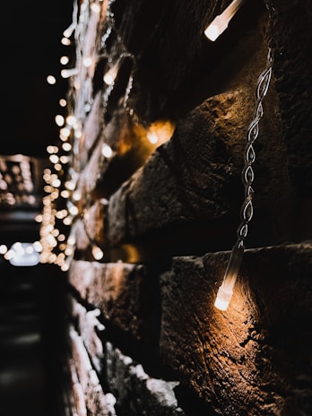 A close-up view of a brick wall adorned with warm white string lights, creating a cozy and inviting atmosphere. The lights are blurred in the background, enhancing the depth and focus on the wall.