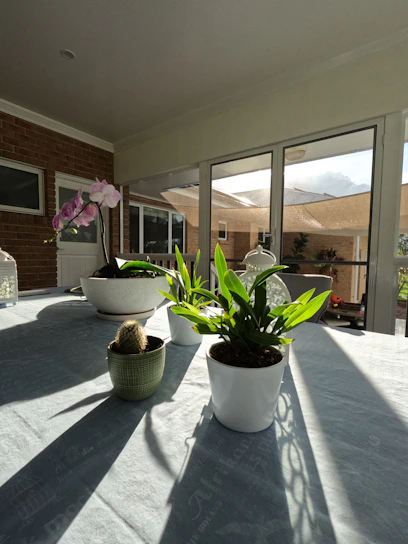 A sunlit patio featuring a plastic outdoor dining chair, terracotta planter with vibrant flowers, and a wooden coffee table.
