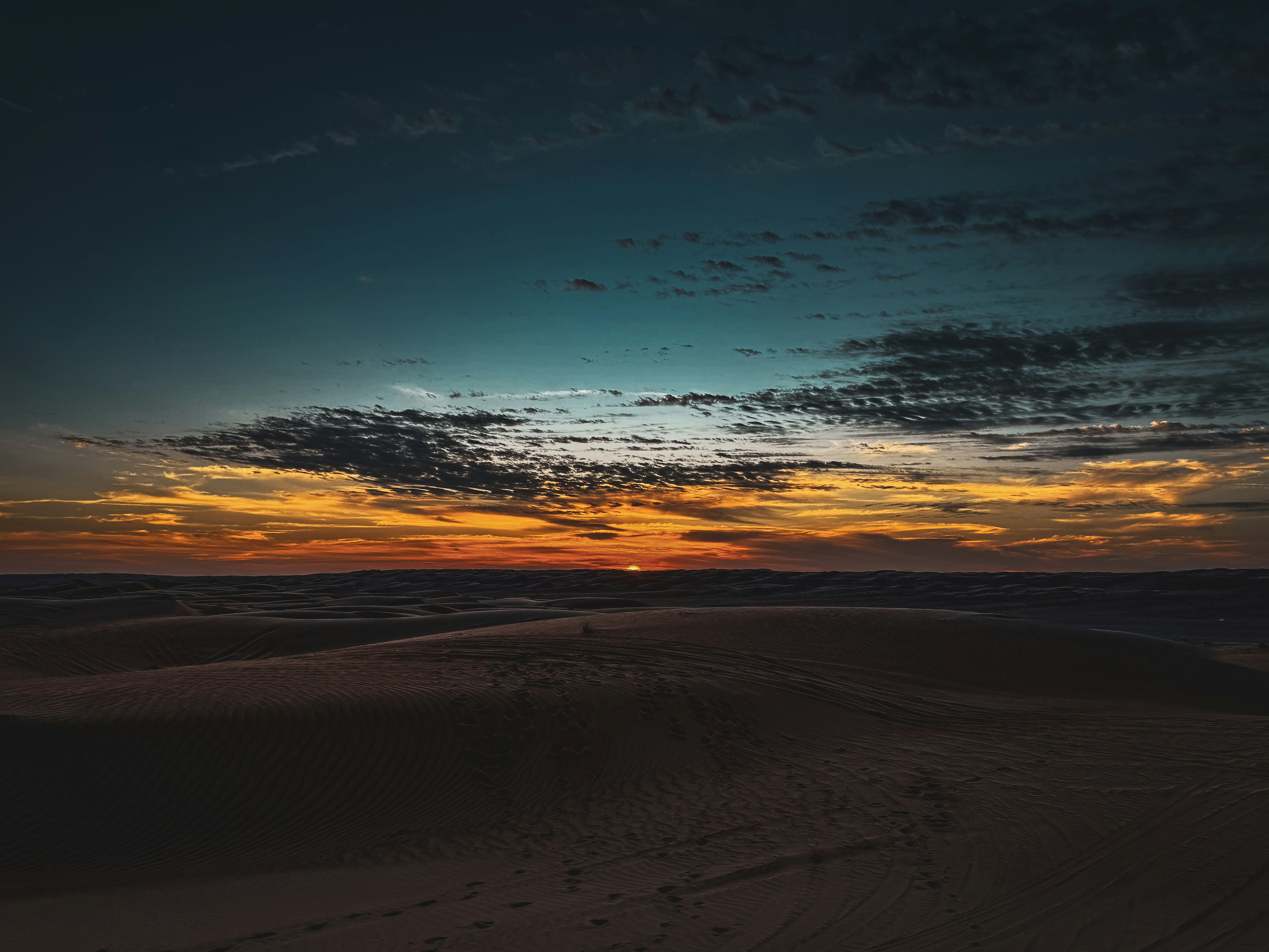 Aerial view of Arabian desert at sunset, perfect parallel dune ridges casting long shadows, deep orange sky