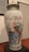 A large, decorative porcelain vase with intricate hand-painted designs featuring colorful birds, elaborate floral patterns, and a detailed landscape scene. The vase has a lid and is displayed on a black pedestal in a gallery setting.