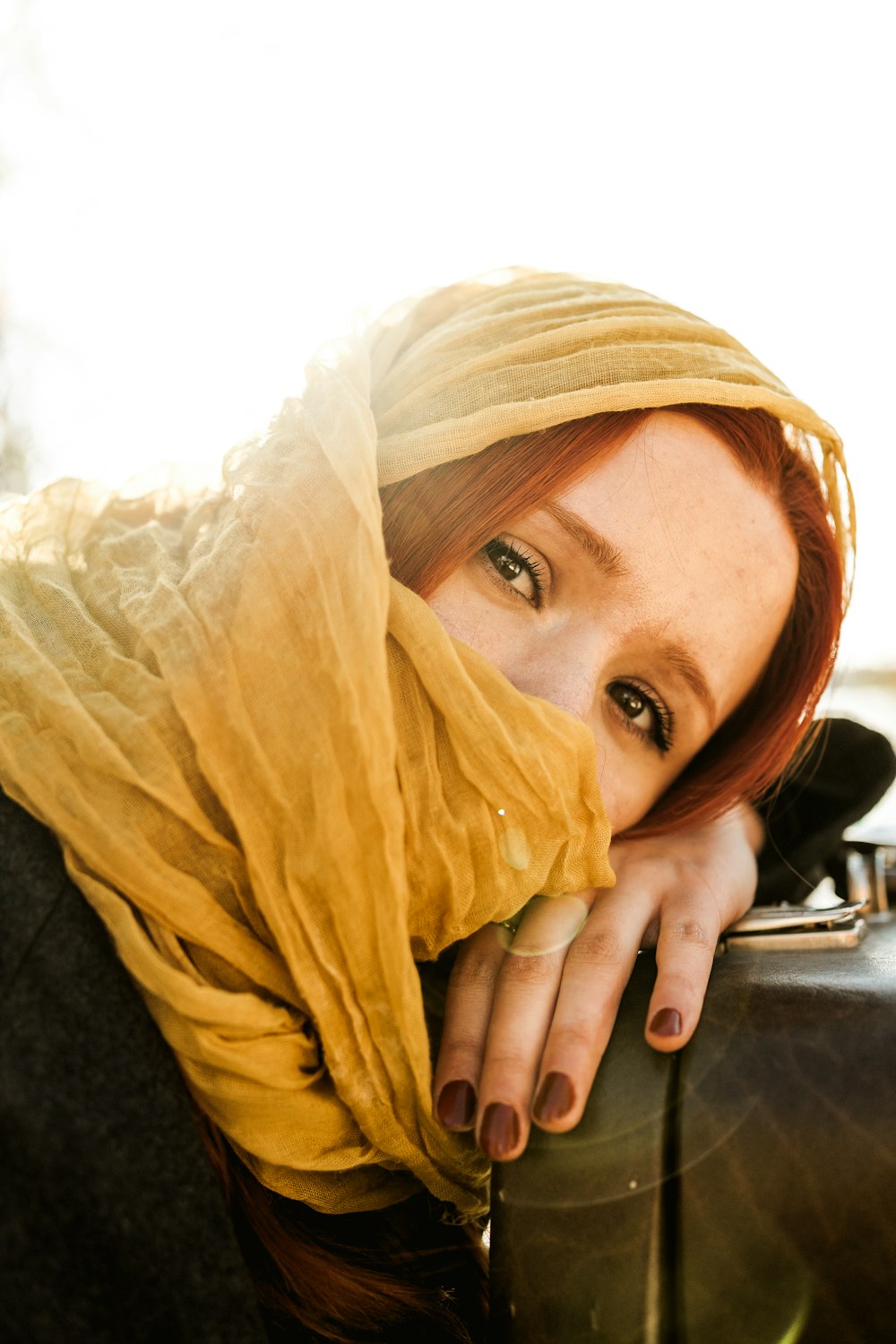 uma mulher com um lenço amarelo na cabeça encostada a uma mala