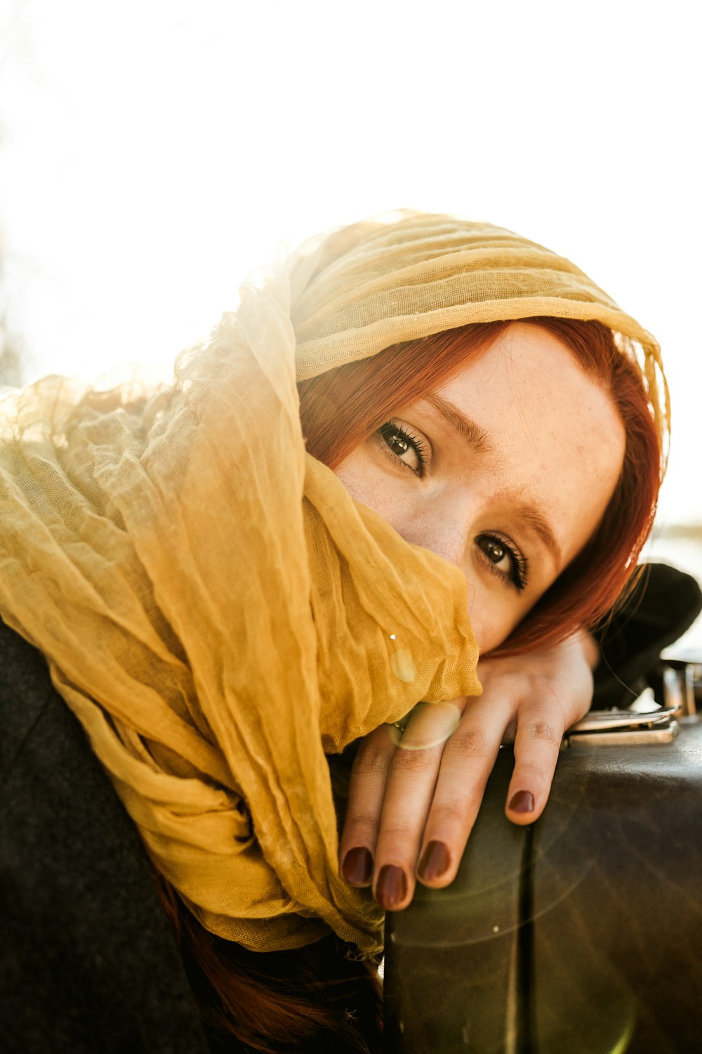 una mujer con un pañuelo amarillo en la cabeza apoyada en una maleta