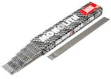 A box labeled 'MONOLITH BASIC' contains a collection of gray welding electrodes. The box has a black and white pattern with a prominent red label. Several electrodes are partially visible, stacked neatly inside the box, while others are laid out side by side in front of it.