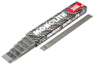 A box labeled 'MONOLITH BASIC' contains a collection of gray welding electrodes. The box has a black and white pattern with a prominent red label. Several electrodes are partially visible, stacked neatly inside the box, while others are laid out side by side in front of it.