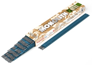 A box of welding electrodes labeled 'MONOLITH' in bold letters. The box has a camouflage pattern and the words 'Welding Electrodes' are clearly visible. Several blue welding rods are partially out of the box and also aligned beside it.