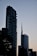 Two modern skyscrapers dominate the skyline against a fading twilight backdrop. The buildings have a sleek and contemporary architectural design, with the structure on the right displaying a logo featuring the name UniCredit. The scene is silhouetted by nearby trees which are partially visible, adding depth to the urban landscape.