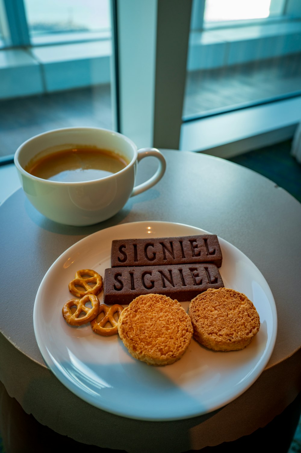 a white plate topped with cookies and pretzels next to a cup of coffee