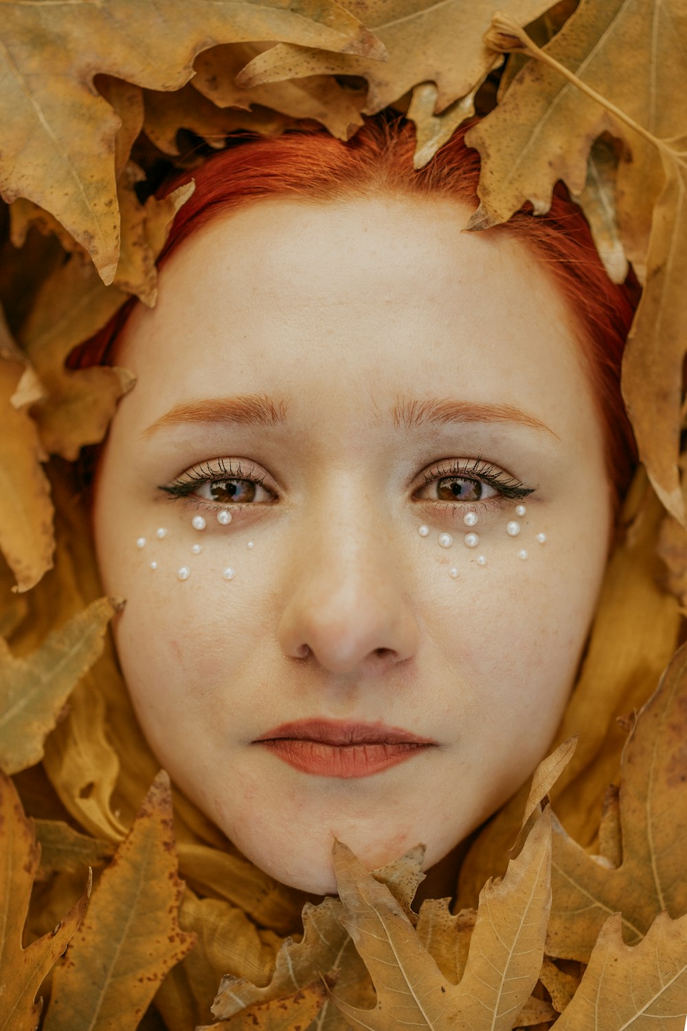 Une femme avec des points blancs sur son visage est entourée de feuilles