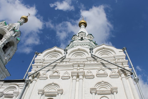 A striking white Orthodox church with intricate architectural details and golden domes set against a bright blue sky. The facade features arched windows and decorative patterns, highlighting traditional Russian design elements.